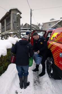 Bombeiros entregam sacos com refeições a idoso, numa estrada cheia de neve.